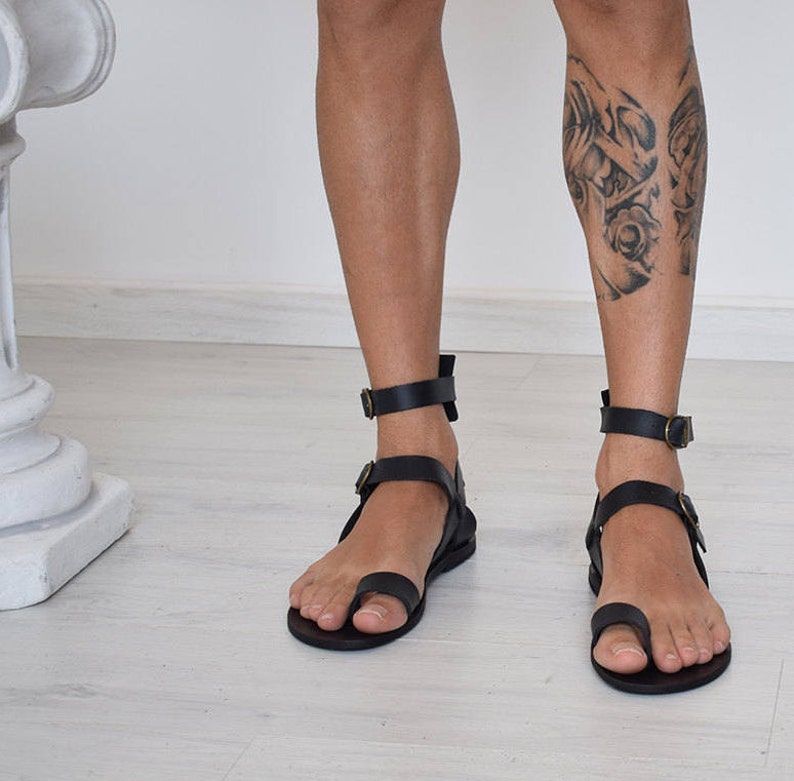 Pode incluir: Sand&aacute;lias de couro preto com uma al&ccedil;a para o dedo do p&eacute; e uma tira para o tornozelo. As sand&aacute;lias t&ecirc;m um design simples e s&atilde;o feitas de couro de alta qualidade.