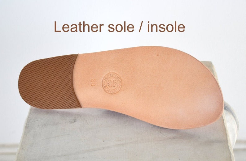 May include: A light brown leather shoe sole with a textured heel and a smooth, rounded toe. The text "Leather sole / insole" is at the top. A circular stamp is visible near the center of the sole.