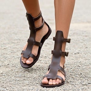 May include: Brown leather gladiator sandals with multiple straps and buckles. The sandals have a toe loop and ankle support, offering a stylish and secure fit. These sandals are a fashionable choice for warm weather.