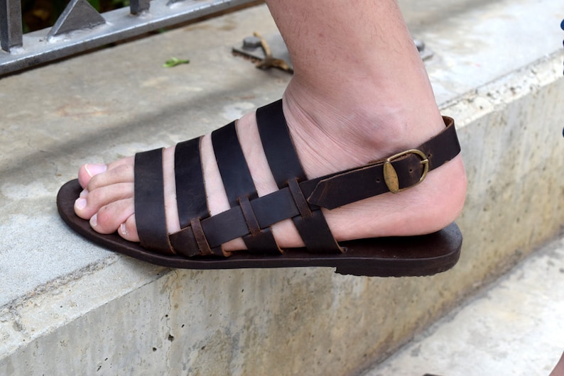 May include: Brown leather sandals with a buckle strap and multiple straps across the foot.