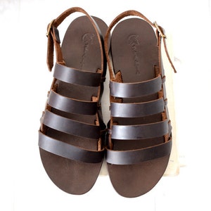 May include: A pair of brown leather sandals with multiple straps. The sandals have a simple design and are made of high-quality leather.