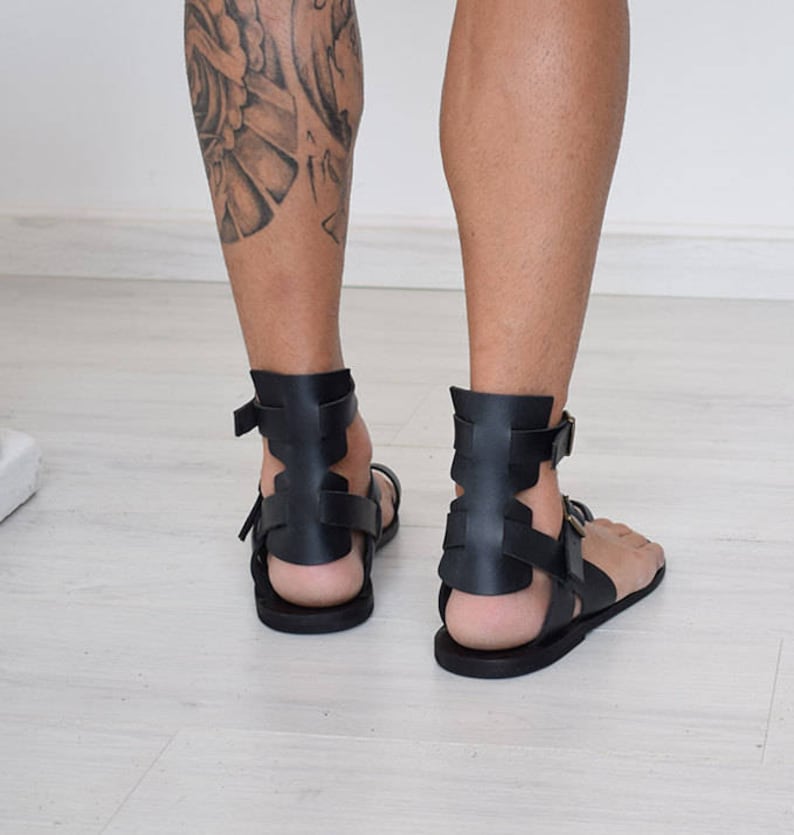 Pode incluir: Sand&aacute;lias de couro preto com um design de estilo gladiador. As sand&aacute;lias t&ecirc;m v&aacute;rias tiras que envolvem o tornozelo e o p&eacute;.
