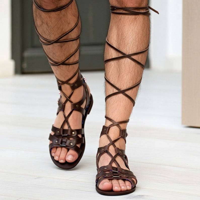 Puede incluir: Sandalias de gladiador en cuero marr&oacute;n oscuro con m&uacute;ltiples tiras horizontales sobre el pie y cordones largos que se envuelven alrededor de la parte inferior de la pierna. Incluyen remaches met&aacute;licos y una suela plana para un ajuste seguro.