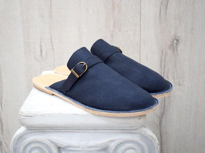 May include: A pair of dark blue leather slip-on shoes with a buckle detail. The shoes have a light brown sole.
