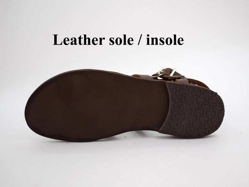 May include: A brown leather sandal with a leather sole and insole. The sandal features a buckle closure and a textured rubber heel. The text "Leather sole / insole" is visible.
