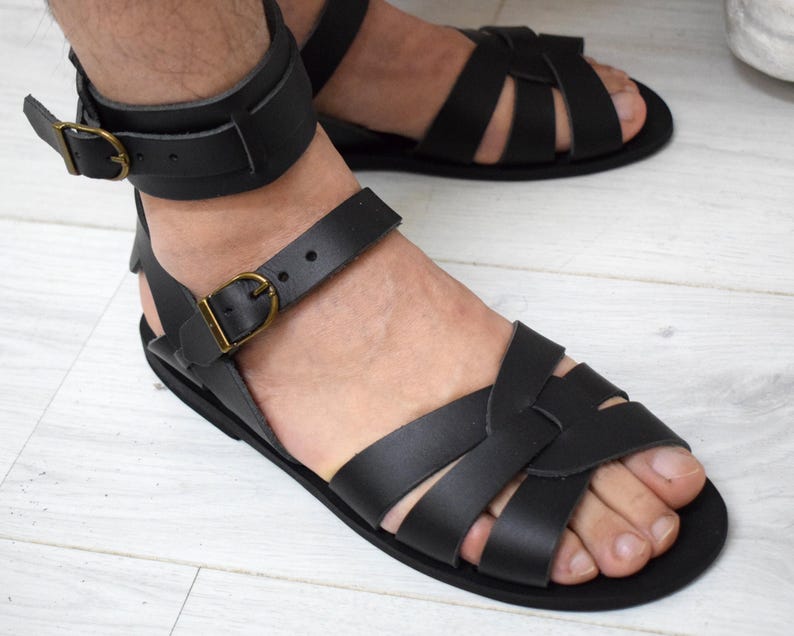 May include: Black leather sandals with multiple straps and ankle straps. The sandals have a flat sole and are secured with adjustable buckles. The design features a classic gladiator style, suitable for warm weather.