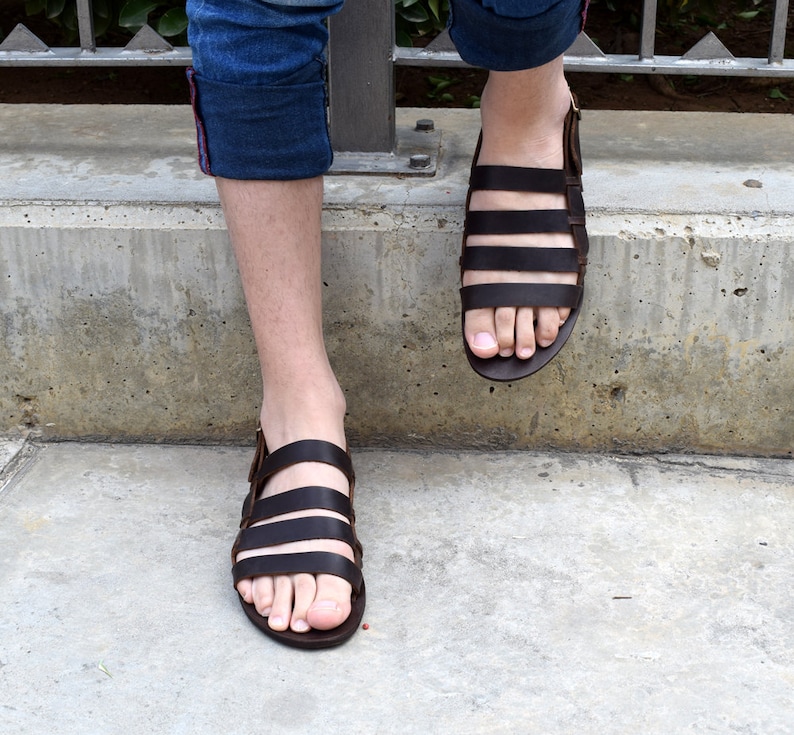May include: Brown leather sandals with multiple straps. The sandals have a simple design and are worn on a person's feet.