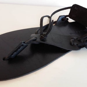 May include: Black leather sandals with a simple design and adjustable straps. The sandals have a flat sole and are made of high-quality leather.