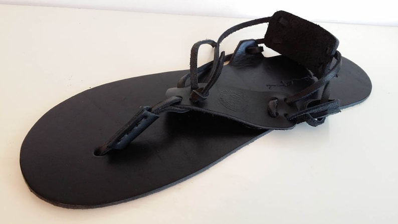 May include: Black leather sandals with a simple design and adjustable straps. The sandals have a flat sole and are made of high-quality leather.