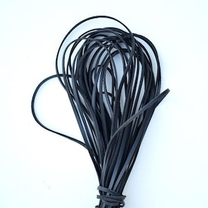 May include: A bundle of black leather strips, tightly bound at the base. The strips are thin and flexible, with a slightly textured surface. The leather appears to be a solid, dark color, and the bundle is set against a plain white background. The strips are likely for crafting or jewelry making.