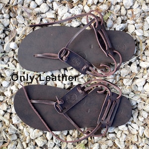 May include: A pair of brown leather sandals with laces that wrap around the ankle. The sandals have a simple design and are made of high-quality leather.