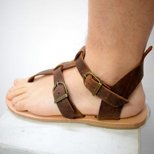 Puede incluir: Sandalias de cuero marr&oacute;n con m&uacute;ltiples correas y hebillas de lat&oacute;n. Las sandalias tienen una suela plana y una correa para el dedo gordo del pie. El cuero parece desgastado, dando a las sandalias un aspecto vintage. C&oacute;modas y con estilo.