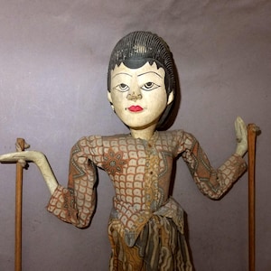 Peut inclure: Marionnette en bois vintage avec un visage peint, des lèvres rouges et des cheveux noirs. La marionnette porte un haut et une jupe marron et beige à motifs. Elle tient des baguettes en bois pour la manipulation.