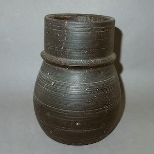 May include: A dark brown, round, ceramic vase with a wide mouth and a slightly flared rim. The vase has a textured surface with horizontal lines.