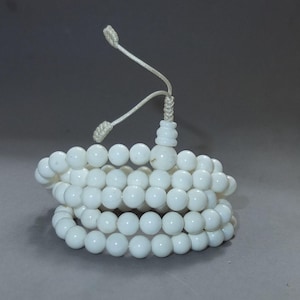 Peut inclure: Un collier de prière mala à perles blanches. Les perles rondes sont enfilées sur un cordon blanc. Le collier est enroulé et possède un pompon. Les perles sont d'une couleur blanche opaque unie.
