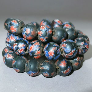Könnte beinhalten: Eine Kette aus schwarzen Glasperlen mit roten, blauen und weißen Blumenmustern. Die Perlen sind rund und haben eine glänzende Oberfläche.