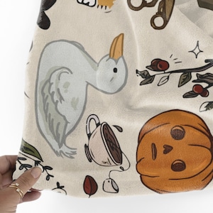 Peut inclure: Un tissu beige avec une vari&eacute;t&eacute; d'illustrations imprim&eacute;es dessus. Les illustrations comprennent un canard, une citrouille, une tasse &agrave; th&eacute;, une branche avec des baies et quelques autres &eacute;l&eacute;ments.