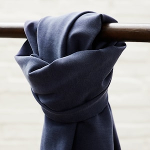 Puede incluir: Primer plano de una tela azul oscuro drapeada sobre una barra de madera. La tela tiene una superficie lisa y ligeramente texturizada.