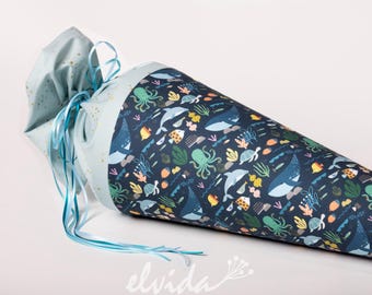 May include: A blue and white fabric cone with a drawstring closure. The cone is decorated with a colourful pattern of sea creatures, including whales, octopuses, fish, and sea turtles. The cone is tied with a light blue ribbon.