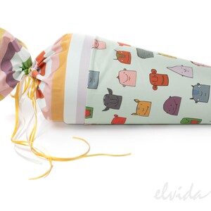 May include: A green and white cone-shaped fabric bag with a colorful striped fabric top. The bag is tied with a yellow ribbon and features a pattern of cartoon faces.