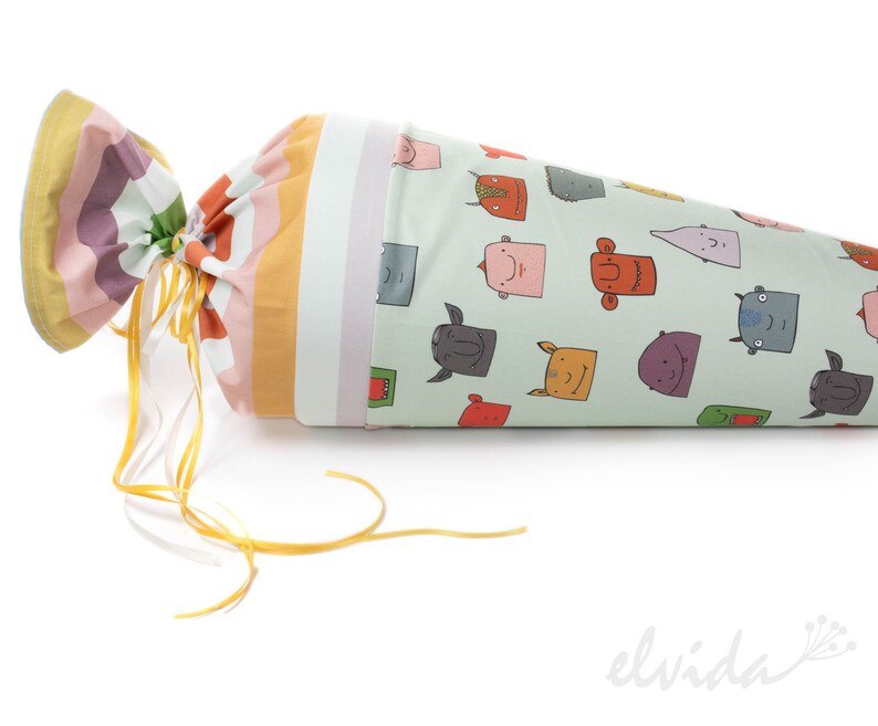 May include: A green and white cone-shaped fabric bag with a colorful striped fabric top. The bag is tied with a yellow ribbon and features a pattern of cartoon faces.