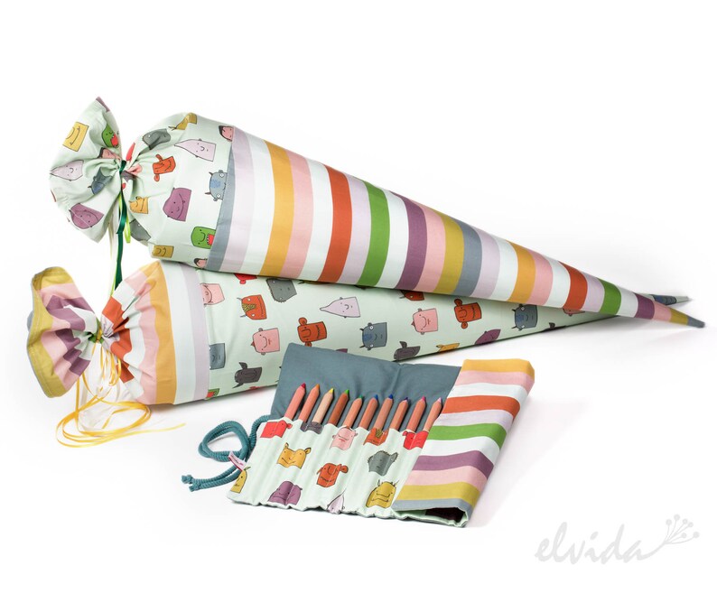 May include: Two colorful striped fabric cones and a matching pencil roll with a green background and cartoon faces. The cones are tied with yellow ribbon and the pencil roll has a blue zipper.