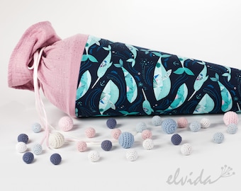 May include: A pink and blue fabric cone-shaped bag with a drawstring closure. The bag is decorated with a pattern of narwhals and stars. The bag is surrounded by small, colorful balls.