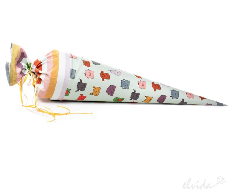 May include: A cone-shaped fabric bag with a yellow ribbon tie. The bag is decorated with a pattern of colorful cartoon faces.