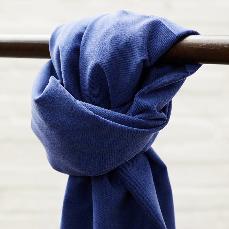 May include: A deep blue fabric scarf is tied around a wooden railing. The fabric is soft and has a slight sheen.