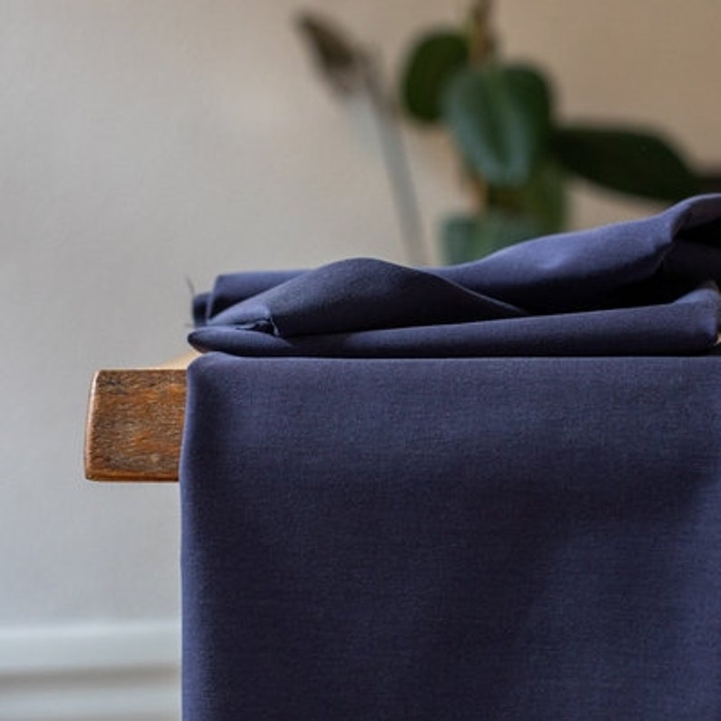 Puede incluir: Primer plano de una tela azul oscuro doblada sobre una superficie de madera. La tela tiene una superficie lisa y ligeramente texturizada.