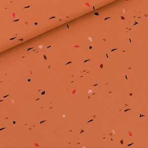 Könnte beinhalten: Orangener Stoff mit einem verstreuten Muster aus schwarzen, roten und rosafarbenen abstrakten Formen.