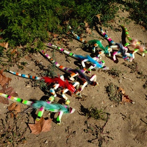 May include: A collection of colorful, segmented, toy lizards with feathered tails. The lizards are arranged in a row on a dirt surface.
