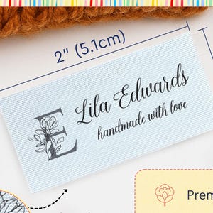 May include: A rectangular light blue cotton label featuring the text Lila Edwards and handmade with love, with a floral letter E. The label measures 2 inches by 1 inch. Text includes Custom Cotton Labels for Handmade Creations and Premium Cotton.