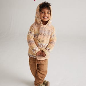 May include: A child wearing a peach, pink and white striped knitted hooded cardigan with brown buttons. The cardigan has a geometric pattern. The child is wearing brown trousers and brown shoes.