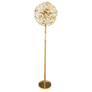 Peut inclure: Un lampadaire doré avec un grand abat-jour rond en verre transparent orné de plusieurs petites sphères dorées. Le lampadaire a un poteau en bois et une base ronde dorée.