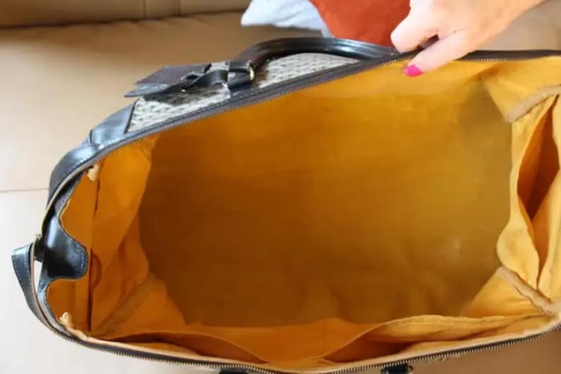 Puede incluir: Una bolsa de viaje negra y marr&oacute;n con forro amarillo. La bolsa tiene cierre de cremallera y un asa superior.