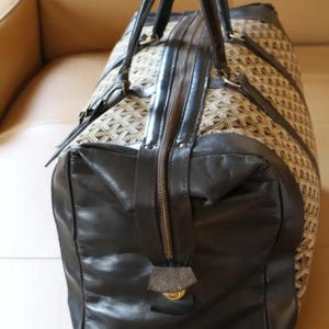 Puede incluir: Una bolsa de viaje de cuero negro y lona marr&oacute;n con cierre de cremallera y dos asas superiores.
