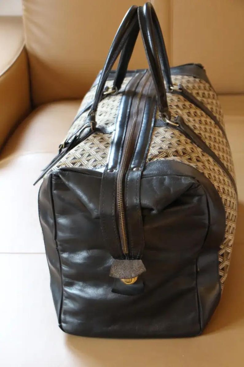 Puede incluir: Una bolsa de viaje de cuero negro y lona marr&oacute;n con cierre de cremallera y dos asas superiores.