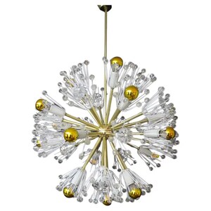 Op de afbeelding: Een gouden en heldere kristallen kroonluchter met een stervormig ontwerp. De kroonluchter heeft meerdere armen met heldere kristallen bollen aan de uiteinden. De kroonluchter hangt aan een gouden ketting.