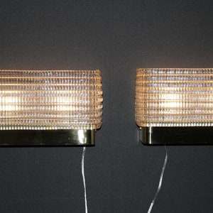 Puede incluir: Par de apliques de pared de lat&oacute;n y vidrio con un patr&oacute;n geom&eacute;trico. Las apliques est&aacute;n iluminadas y tienen un brillo c&aacute;lido.