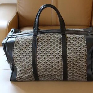 Puede incluir: Una bolsa de viaje negra y marr&oacute;n con un patr&oacute;n geom&eacute;trico. La bolsa tiene dos asas superiores y un cierre de cremallera.