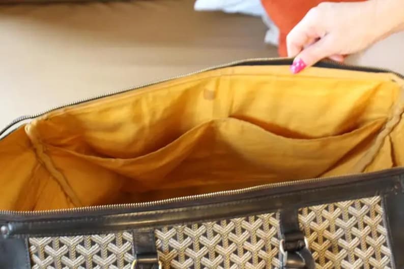 Puede incluir: Una bolsa de viaje marr&oacute;n y negra con forro amarillo y varios bolsillos. La bolsa tiene un patr&oacute;n geom&eacute;trico en el exterior.
