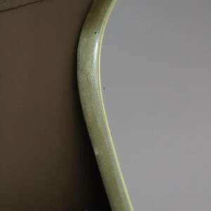 May include: A curved, light yellow object with a textured surface, possibly a frame or trim, against a tan and gray background. The object has a slight sheen and a subtle pattern.