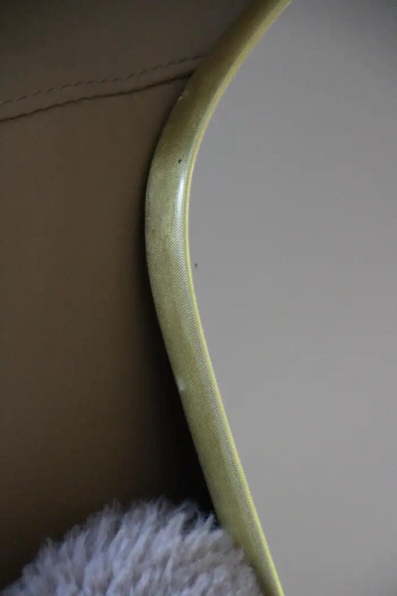 May include: A curved, light yellow object with a textured surface, possibly a frame or trim, against a tan and gray background. The object has a slight sheen and a subtle pattern.