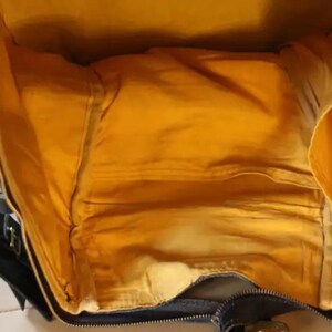 Puede incluir: Una bolsa de viaje negra y marr&oacute;n con un forro de tela amarillo. La bolsa tiene una cremallera y un asa.