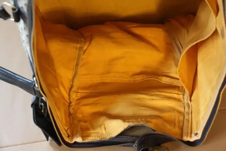 Puede incluir: Una bolsa de viaje negra y marr&oacute;n con un forro de tela amarillo. La bolsa tiene una cremallera y un asa.