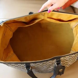 Puede incluir: Una bolsa de viaje vac&iacute;a marr&oacute;n y negra con forro amarillo. La bolsa tiene cierre de cremallera y asa.