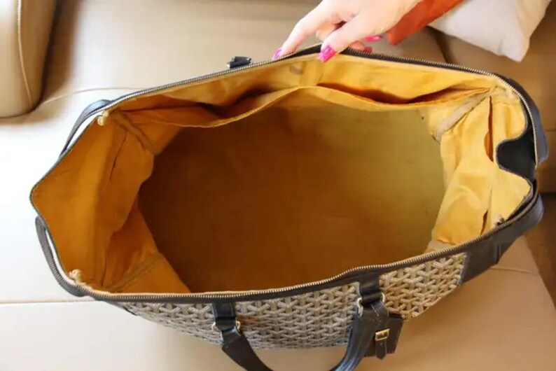 Puede incluir: Una bolsa de viaje vac&iacute;a marr&oacute;n y negra con forro amarillo. La bolsa tiene cierre de cremallera y asa.