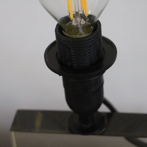May include: Close-up of a black lamp socket with a clear light bulb inserted. The socket has a decorative ring around the base.