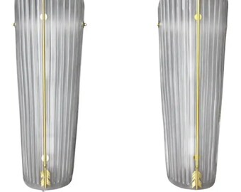 May include: Pair of clear glass wall sconces with gold arrow accents. The sconces have a fluted design and are mounted on a wall.